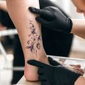 Person getting a tattoo of flowers over their spider veins
